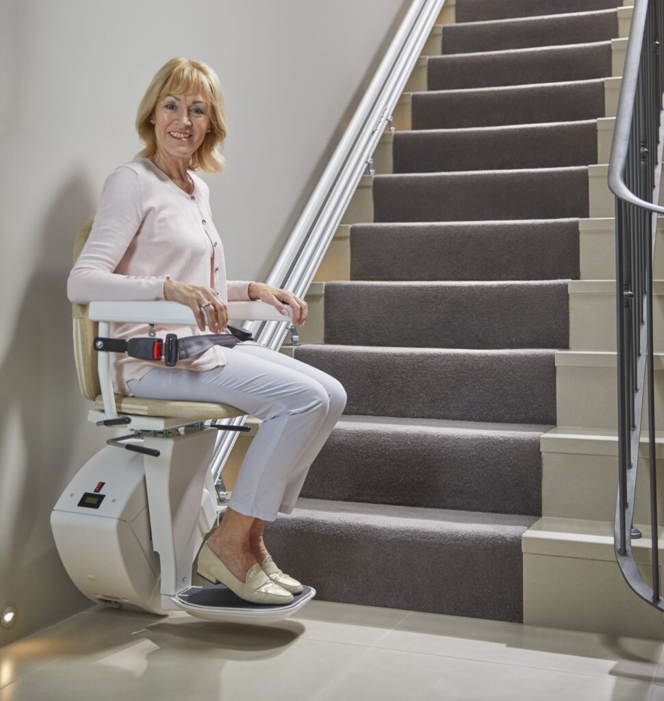 Older women seated on a stairlift beside an indoor staircase
